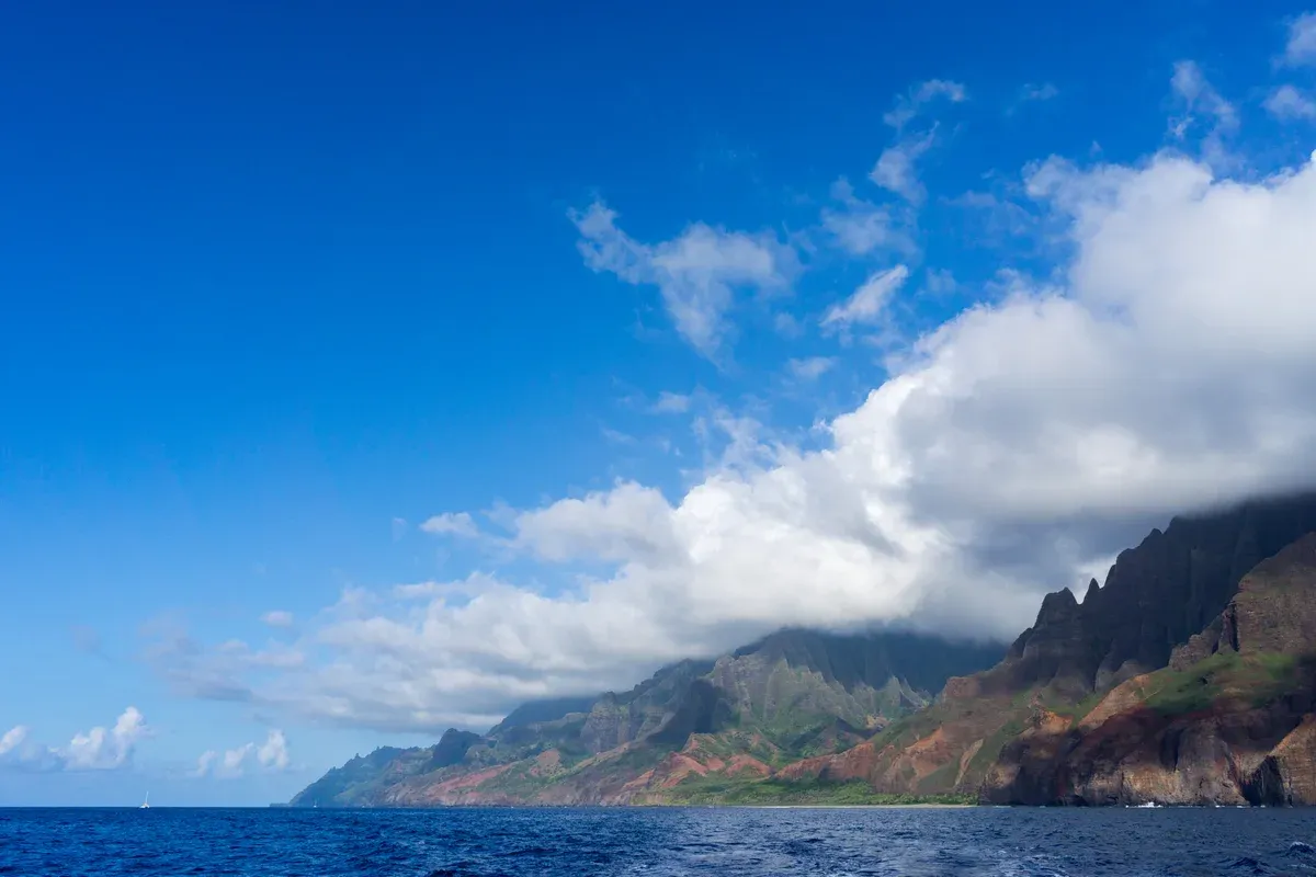 Blue water and cloud-topped cliffs along the Na Pali Coast on a Kauai boat cruise